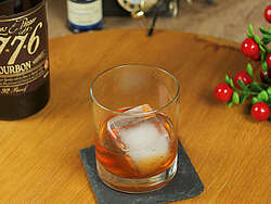 The Old Fashioned cocktail in a tumbler with an ice cube, a bottle of 1776 whisky and decoration